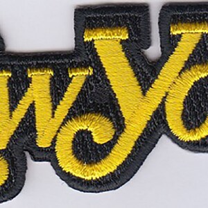 May include: A yellow embroidered patch with the word "NEW YORK" in a stylized font on a black background.