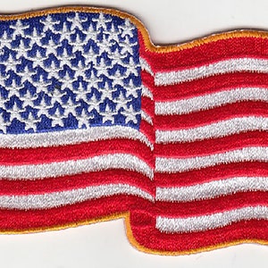 May include: A red, white, and blue American flag patch with a gold border. The flag is waving in the wind.