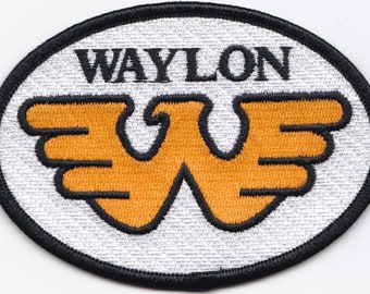 May include: Oval patch with the name "WAYLON" in black, above a stylized orange and black design. The patch has a black border and a silver background.