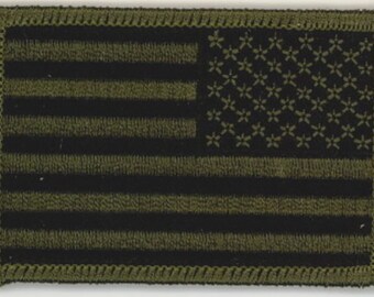 May include: A rectangular patch featuring the American flag in black and olive green. The flag design includes horizontal stripes and a field of stars. The patch has a stitched border.