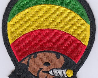 May include: Embroidered patch featuring a cartoon character with a red, yellow, and green hat, wearing a black bandana and smoking a cigarette. The character has brown skin and black hair.