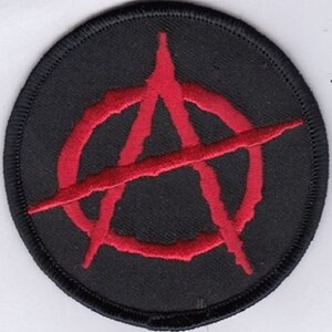 May include: A black and red embroidered patch with an anarchy symbol. The symbol is a circle with an 'A' inside, with a diagonal line through it.