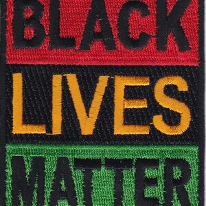 May include: Black Lives Matter patch with red, yellow, and green embroidered text on a black background.