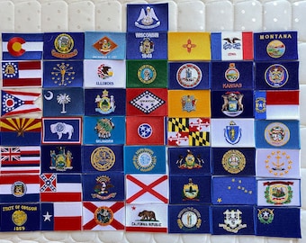 May include: A collection of 36 embroidered patches featuring the state flags of the United States. Each patch is rectangular and has a white background with the state flag design in colorful embroidery. The patches are arranged in six rows of six, with the state name and year of statehood printed below each flag.