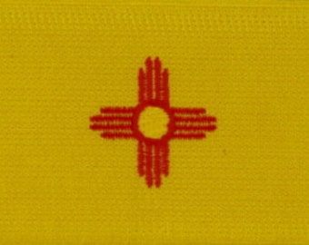 May include: A rectangular patch featuring the New Mexico state flag. The flag has a bright yellow background with a central red Zia symbol. The Zia symbol is a circle with four groups of four rays extending outward.