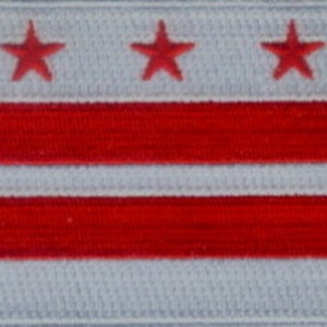 May include: Embroidered patch featuring the flag of Washington, D.C. The design includes three red stars on a white background at the top, with two red horizontal stripes separated by a white stripe below. The patch has a textured appearance.