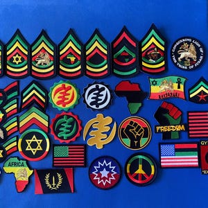 May include: A collection of embroidered patches with various designs and symbols. The patches feature Rastafarian, Pan-African, and freedom-themed imagery, including flags, stars, and the word "FREEDOM". The color palette includes green, yellow, red, and black.