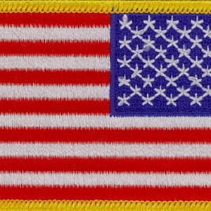 May include: A small embroidered American flag patch with a yellow border. The flag has 13 red and white stripes and a blue field with 50 white stars.