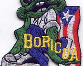 May include: An embroidered patch featuring a cartoon frog wearing blue jeans and a white shirt, leaning against a red, white, and blue flag with a white star. The text "BORICUA" is embroidered in yellow on the patch.