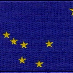 May include: The flag of Alaska features a blue background with eight gold stars arranged in the shape of the Big Dipper constellation.