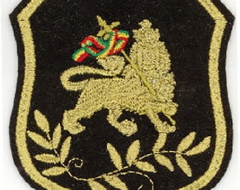 May include: A black embroidered patch with a gold lion holding a flag with red, green, and yellow stripes. The lion is surrounded by a gold laurel wreath.