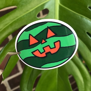May include: A green and orange Halloween jack-o'-lantern sticker with a wavy pattern.