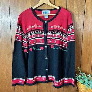May include: A button-up cardigan in red and black with floral embroidery. The sweater features a round neckline, long sleeves, and a pattern of roses and stripes. The brand label "BFA" is visible at the top.