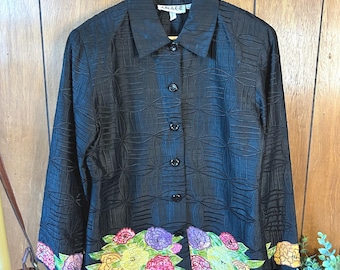 May include: Black button-down jacket with a floral design at the hem and cuffs. The jacket has a textured pattern and a collar. The floral design includes pink, yellow, purple, and green colors. The jacket is hanging on a wooden hanger.