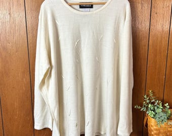 May include: Cream-colored long-sleeve sweater with a crew neck and subtle embroidered leaf design. The sweater is hanging on a wooden hanger against a wood-paneled wall. The brand name is visible on the neckline.