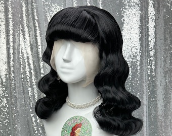 May include: A black wig with long, loose curls and a fringe. The wig is styled in a vintage 1940s or 1950s style. The wig is on a white mannequin head.