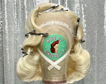 May include: A blonde wig on a wig stand with a green circle label that says "Wigs By Gingerella".