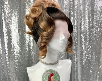 May include: A two-toned wig with a light brown and dark brown color scheme, styled with voluminous curls and a high bun. The wig is displayed on a white mannequin head with a rhinestone necklace. The mannequin has a sticker that says "Wigs by Cinderella".