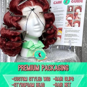 May include: A styled auburn wig on a styrofoam head, secured with hair clips and a hair net. The wig is part of a premium packaging set that includes a care guide, pins for storage, a wig cap, and a free sticker. The packaging is labeled "Premium Packaging".