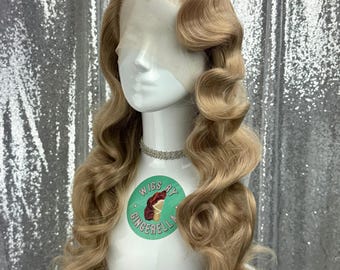 May include: A light blonde wig with long, voluminous curls styled in a vintage wave pattern. The wig is displayed on a white mannequin head with a delicate silver necklace. The mannequin has a sticker that says "Wigs by Gingerella".