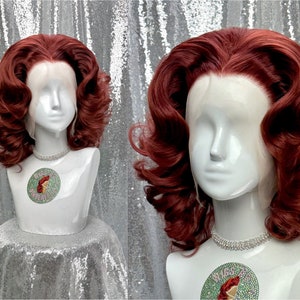 以下が含まれることがあります： 白いマネキンの頭に展示された、ボリュームのあるカールしたレイヤーの赤褐色のかつら。 かつらはレースフロントが特徴で、ヴィンテージで華やかなスタイルです。 ラインストーンのネックレスがマネキンの首を飾っています。