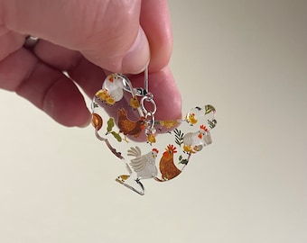 Peut inclure: Une paire de boucles d'oreilles en acrylique transparent en forme de poulet avec un motif de poulet blanc et brun. Les boucles d'oreilles ont des crochets argentés.