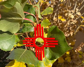 Peut inclure: Un symbole rouge stylisé du symbole du soleil Zia, un symbole traditionnel du peuple Pueblo du Nouveau-Mexique, suspendu à une branche d'arbre.