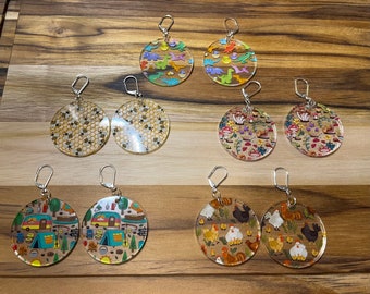 Peut inclure: Assortiment de 10 paires de boucles d'oreilles rondes en acrylique transparent avec différents motifs colorés. Les motifs comprennent des abeilles, des dinosaures, des champignons, des campeurs et des poulets.