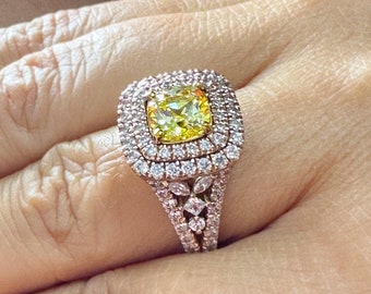 May include: A gold ring with a large, square-shaped yellow diamond surrounded by smaller diamonds. The ring has a double halo setting and a delicate band.