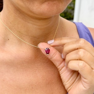 May include: A gold chain necklace with a teardrop-shaped red gemstone pendant.