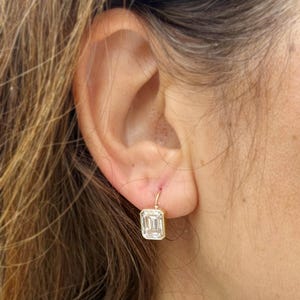 Peut inclure: Une paire de boucles d'oreilles en or avec une seule grande pierre précieuse transparente de taille émeraude suspendue à chaque boucle.