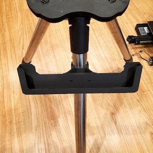 May include: A black tripod with a silver center pole and a black tray attached to the pole. The tripod has a black base with three legs.