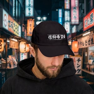 May include: Black baseball cap with white Japanese characters. The cap has a curved brim and a simple, classic design. The text is centered on the front of the cap.