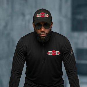 May include: A black baseball cap and a black long-sleeve quarter-zip pullover. Both items feature a red circular emblem with white horizontal bars and black Japanese characters that read 信仰希望愛. The pullover has a small white logo on the sleeve.