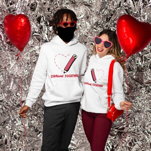 May include: Two white hoodies with a red heart and pencil design. The text on the hoodies says "Drawn Together".