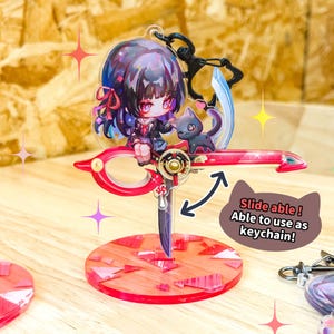 May include: A red and gold acrylic keychain featuring an anime-style character with a black cat. The keychain has a scissor-like design with a red base and the text "Slide able! Able to use as keychain!"