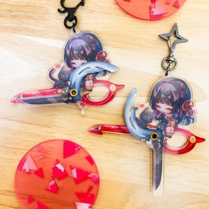 May include: Two anime-style keychains featuring a girl with dark hair and a black cat, holding a stylized weapon. The keychains have a red, blue, and white color scheme. Also, two red coasters with pink geometric shapes and a black cat keychain.