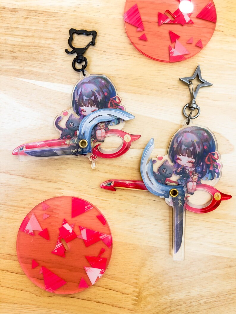 May include: Two anime-style keychains featuring a girl with dark hair and a black cat, holding a stylized weapon. The keychains have a red, blue, and white color scheme. Also, two red coasters with pink geometric shapes and a black cat keychain.