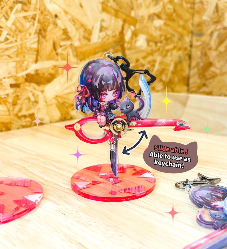May include: A red and gold acrylic keychain featuring an anime-style character with a black cat. The keychain has a scissor-like design with a red base and the text "Slide able! Able to use as keychain!"