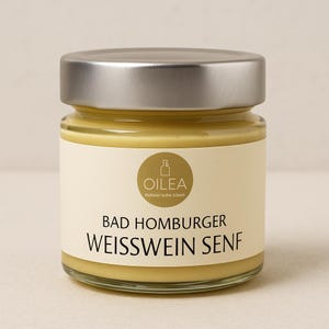 Op de afbeelding: Een klein glazen potje gele mosterd met een zilveren deksel. Het etiket leest "Oilea" en "Bad Homburger Weisswein Senf". De pot is gevuld met een gladde, romige mosterd.