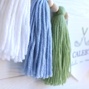 May include: A handmade banner with white, light blue, and green yarn tassels. The banner includes wooden beads and a white pennant with the text "Caleb's" and golf-themed graphics.