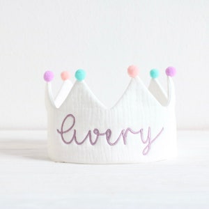 May include: White felt crown with purple pom-poms and the name "Avery" embroidered in purple thread.