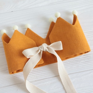 May include: A yellow felt crown with white pom-poms and a white satin ribbon tied in a bow.
