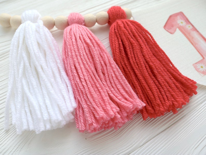 Puede incluir: Tres borlas de hilo en blanco, rosa y rojo colgando de una varilla de madera. Las borlas est&aacute;n hechas de hilo suave y esponjoso y son perfectas para agregar un toque de fantas&iacute;a a cualquier espacio.