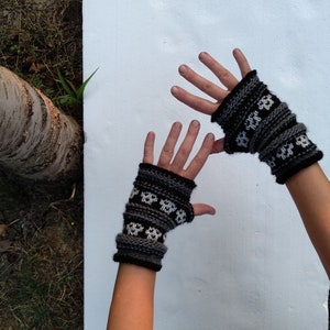 May include: A pair of black and white fingerless gloves with a skull pattern. The gloves are knitted and have a striped design.
