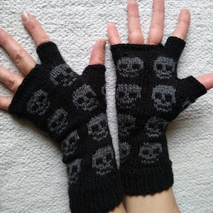 May include: A pair of black fingerless gloves with a gray skull pattern. The gloves are knitted and have a ribbed cuff.