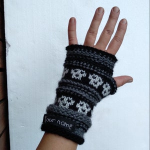 May include: Black and white knit fingerless gloves with a geometric pattern. The gloves have a black tag with the text "Your name" on them.