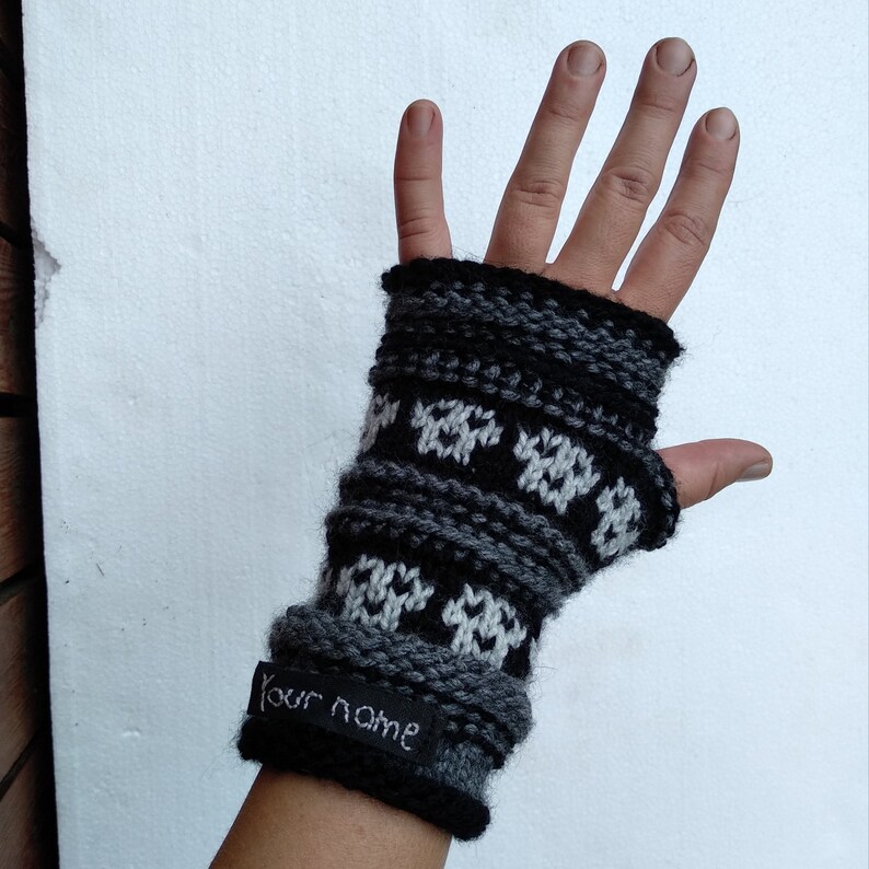 May include: Black and white knit fingerless gloves with a geometric pattern. The gloves have a black tag with the text "Your name" on them.