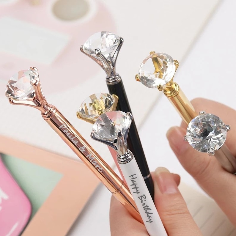 May include: Four diamond-shaped pens with different colored metal accents. The pens have personalized inscriptions, including "Happy Birthday" and "Paula & Marc".