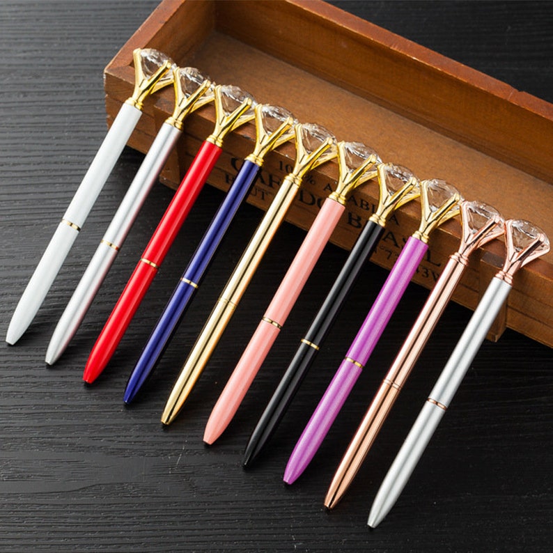 May include: A set of ten pens with a diamond-shaped top. The pens are silver, gold, black, red, blue, pink, purple, and rose gold.